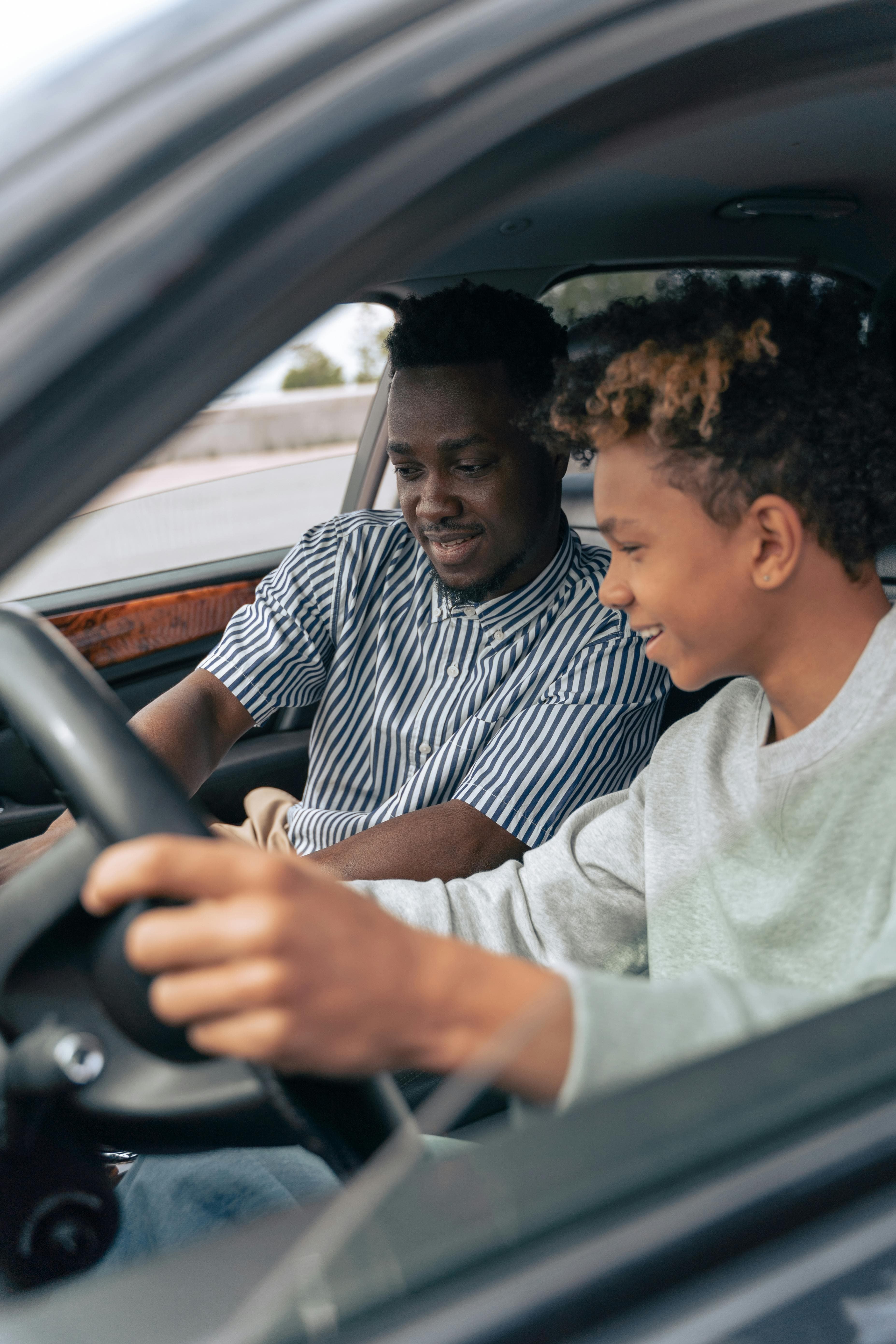 Un padre y su hijo al volante juntos, las manos del niño sobre el volante